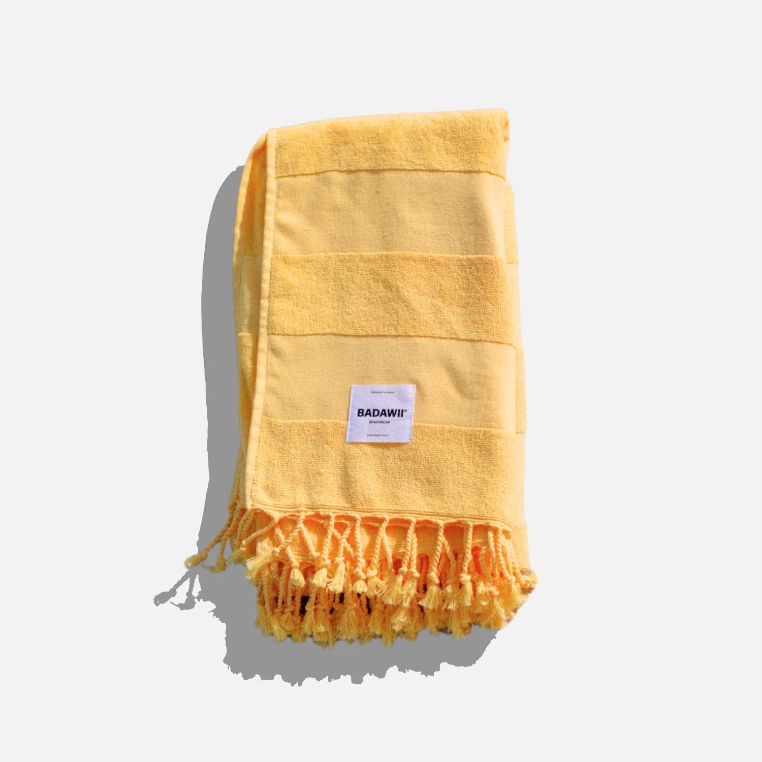Yellow towel with fringes and a brand label on a white background