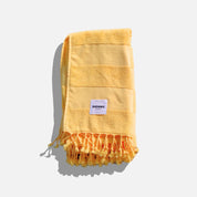 Yellow towel with fringes and a brand label on a white background
